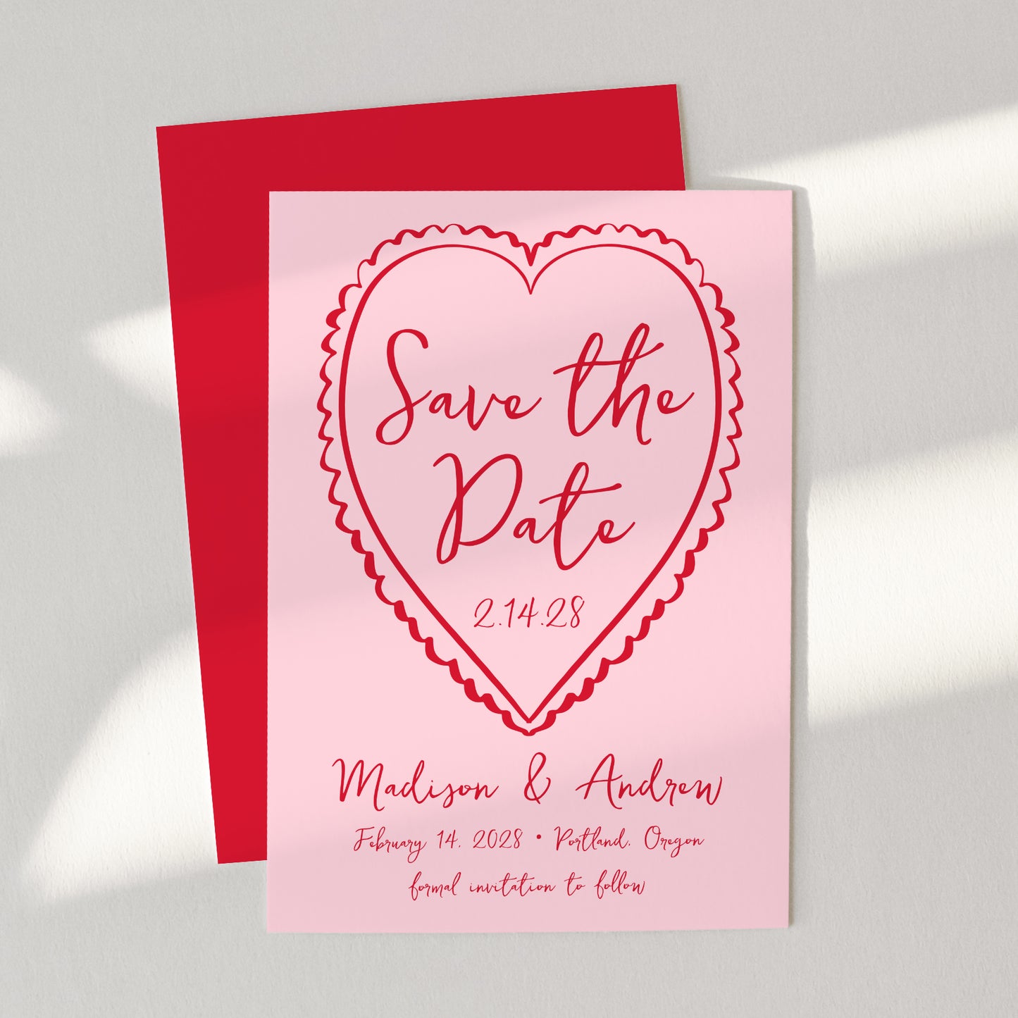 Pink 'Save the Date' card with red heart design on a gray background